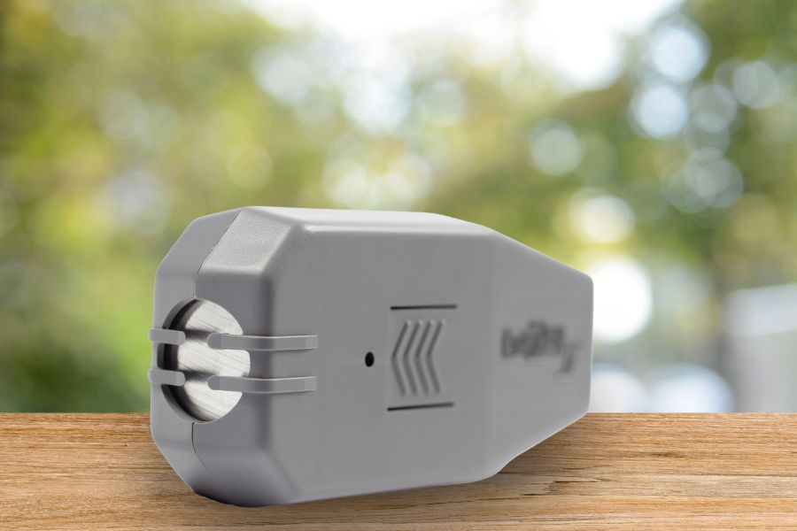 Close-up of the Dazer 2 ultrasonic dog repellent. The device stands on a wooden countertop, with greenery in the background.