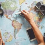 The graphic depicts preparations for a trip: a map, a notebook in one hand, an airplane in the other, and a compass and coffee nearby.